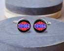 A pair of stainless steel cufflinks with the Toyoda logo on a wooden surface.